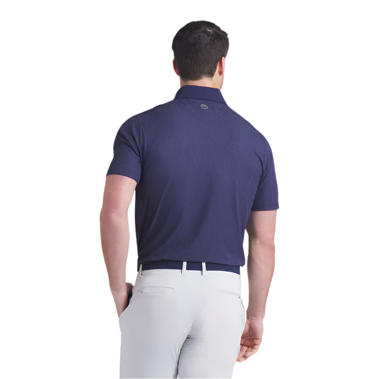 Man wearing a navy blue polo shirt and white pants on a light gray background