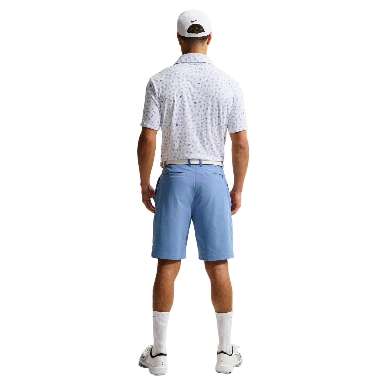 Man wearing a patterned polo shirt, blue shorts, and white cap on a light gray background