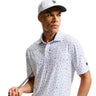 Man wearing a white patterned polo shirt and cap, holding a golf club on a light background
