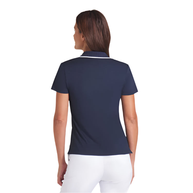 Woman wearing a navy polo shirt with white pants on a light gray background