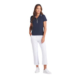 Woman wearing a navy polo shirt and white pants on a light gray background