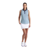 Woman wearing a sleeveless patterned top and white skirt on a light gray background